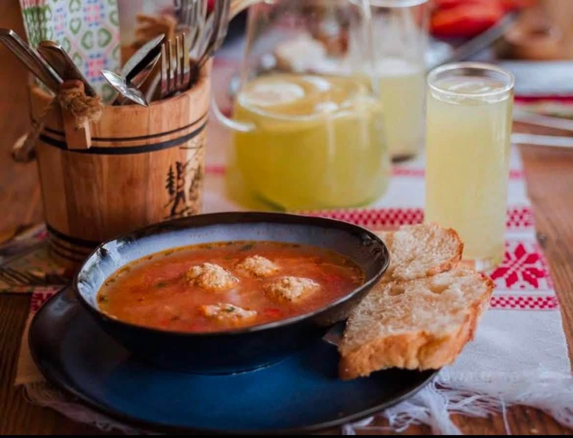 Ciorbă de perișoare într-un bol albastru, cu pâine de casă și limonadă, pe o față de masă tradițională