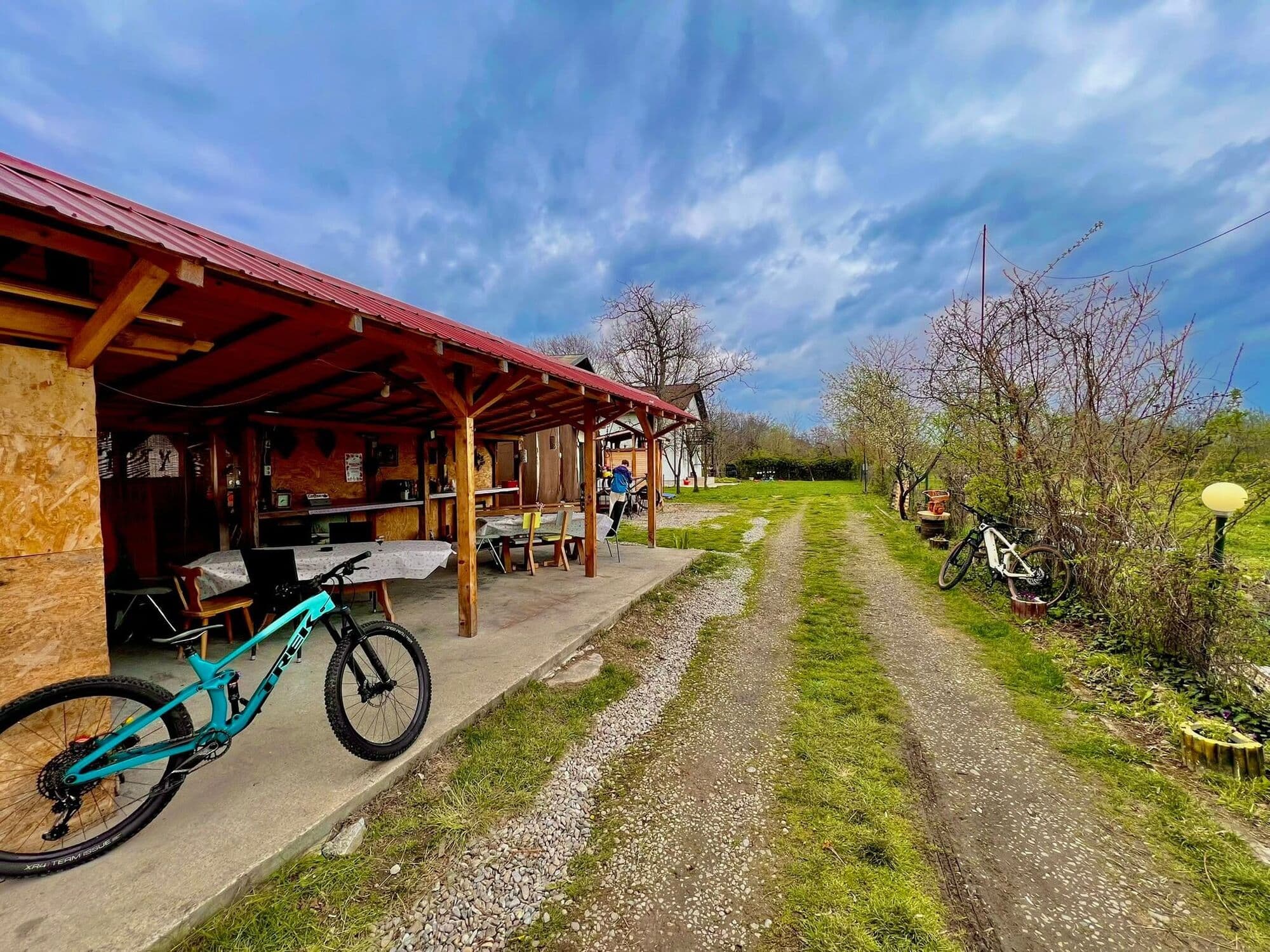 Foișorul din lemn cu acoperiș roșu de la Cerbu Bike Inn, cu o bicicletă de munte turcoaz lângă aleea pietruită