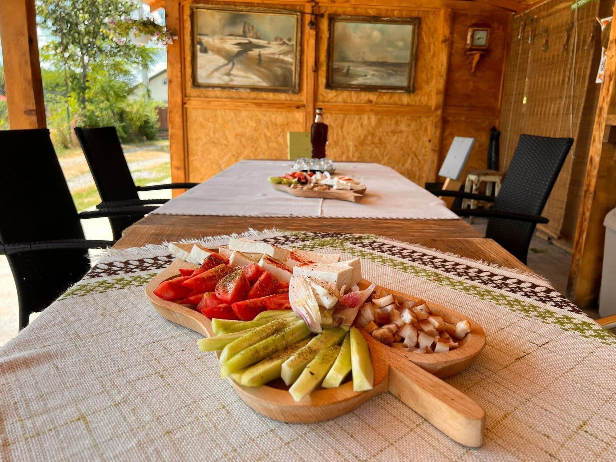 Platou de lemn cu legume tăiate, brânzeturi și mezeluri pe masa de sub foișor